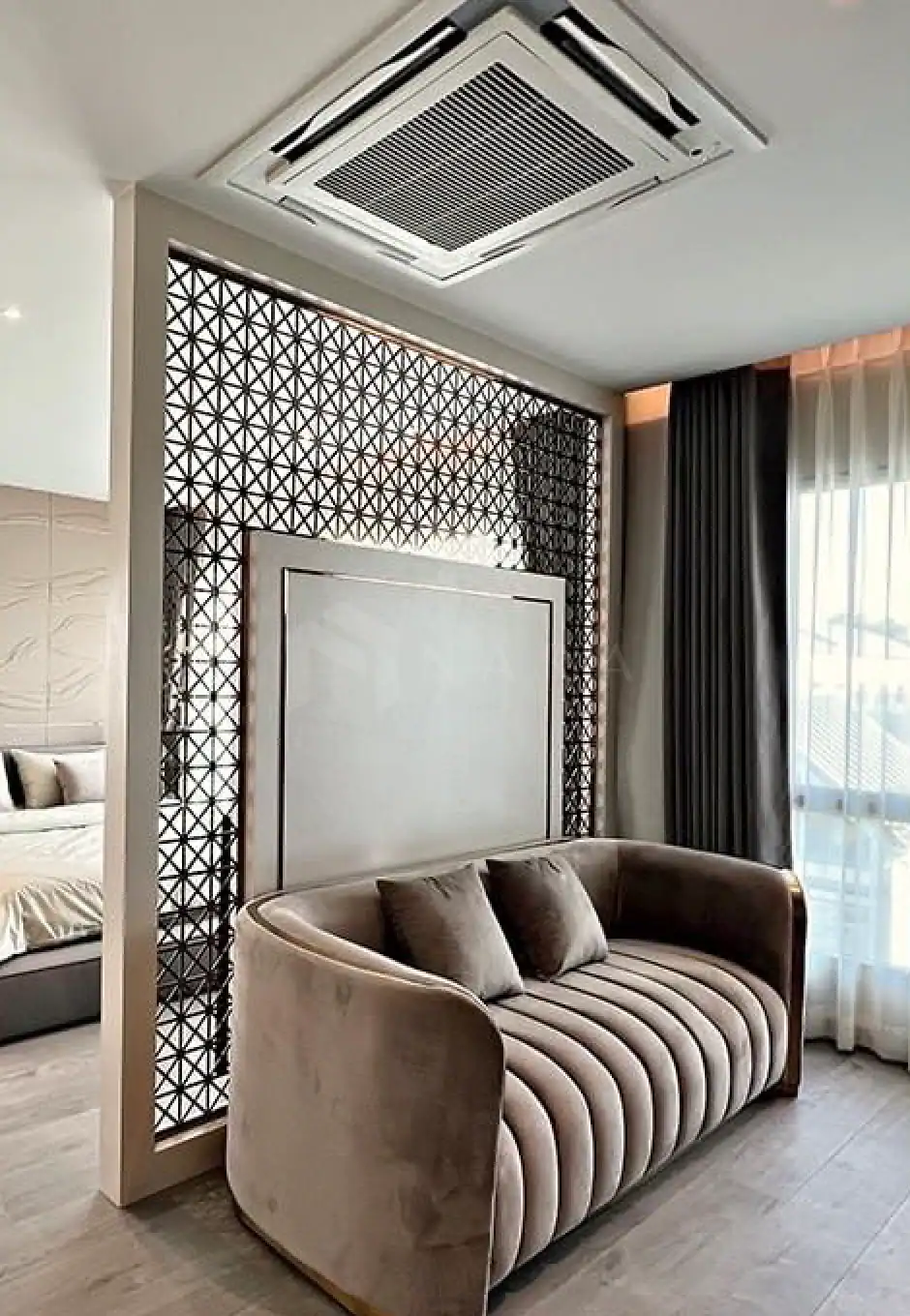 Shiny gold stainless steel decorative corner trim in modern living room interior with a plush beige velvet sofa, sheer curtains, and intricate geometric wall accents.