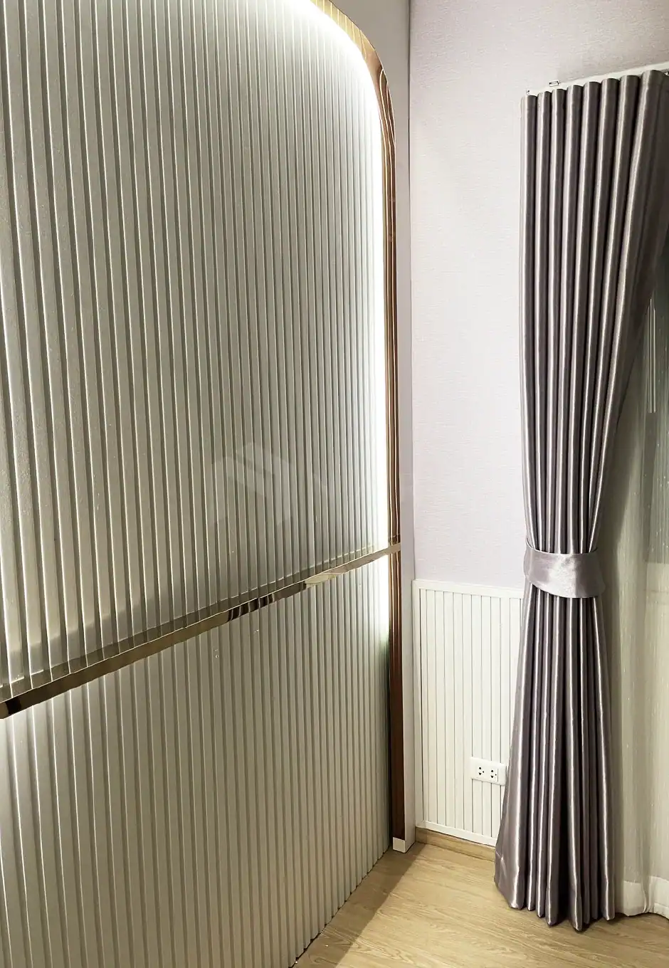 Polished gold-colored stainless steel decorative edge profile with vertical ridges, installed in a modern interior space, adding elegance and contemporary style to the room.