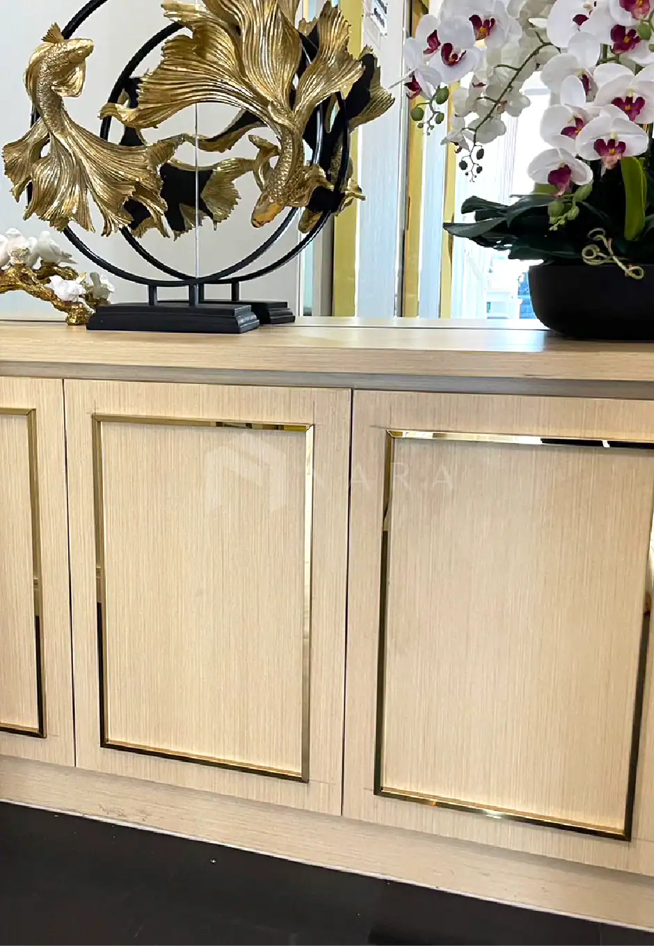 Shiny gold stainless steel decorative trim on beige wooden cabinet with floral ornament and flower pot, showcasing elegant stainless steel accents for home decor and interior design.