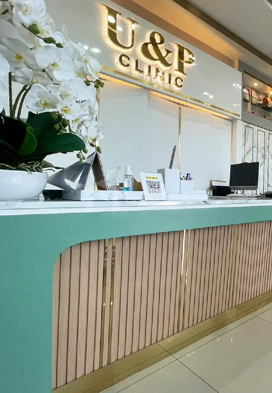 Shiny gold-colored stainless steel Trim for interior decor at U&P Clinic reception with white orchid flower arrangement, modern design, and elegant finishes. Perfect for luxurious clinics or offices.