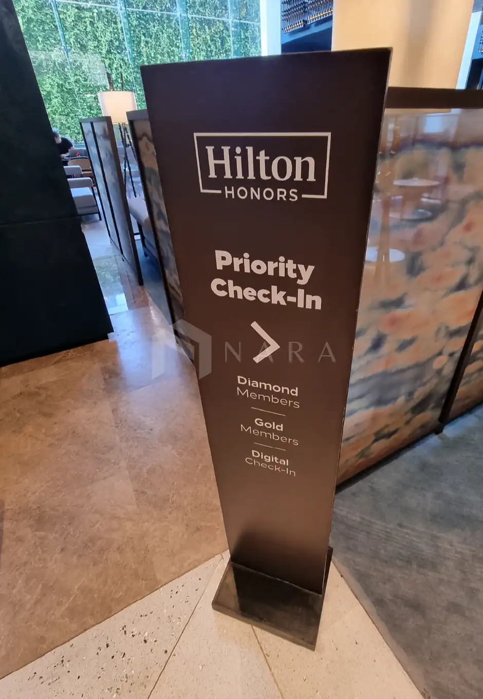 Acrylic black hotel priority check-in sign at Hilton Honore, showcasing diamond, gold, and digital member check-in options, placed in a luxurious hotel lobby environment.