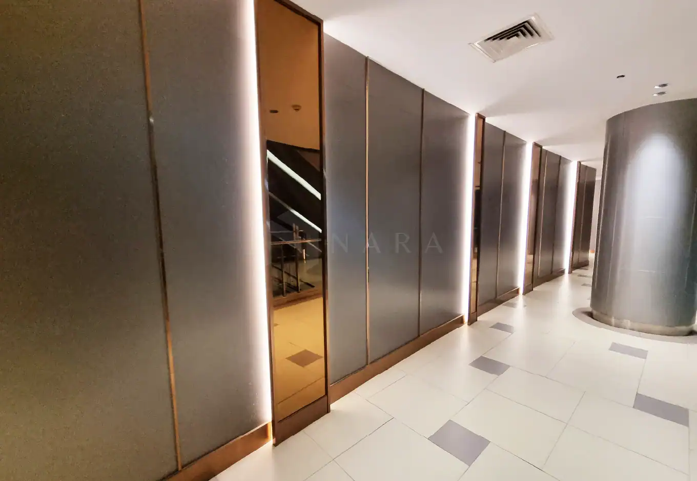 Shiny gold-colored stainless steel trim and decorative panels in a modern building corridor with soft lighting and elegant design elements.