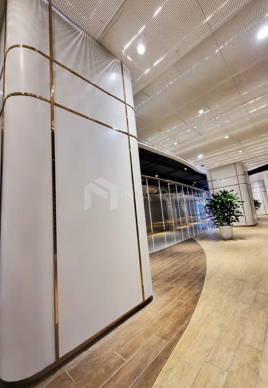 Shiny gold stainless steel corner trim accents modern office interior, adding elegance and sophistication to the sleek white wall panels and curved ceiling design.
