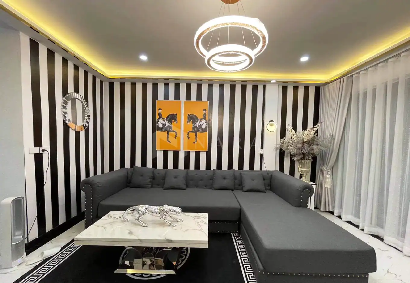 Luxurious living room with gold-colored stainless steel decorative trims, contemporary black-and-white striped feature wall, elegant chandelier, and stylish furnishings for sophisticated interiors.