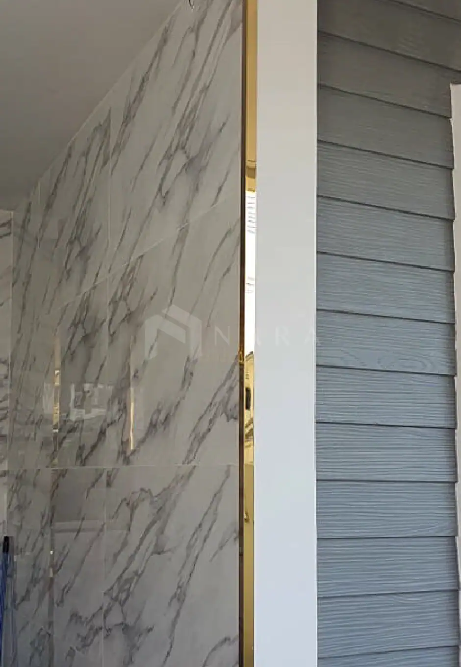Brushed gold stainless steel trim used as decorative edging between the marble wall and grey shutter panels in modern interior design.