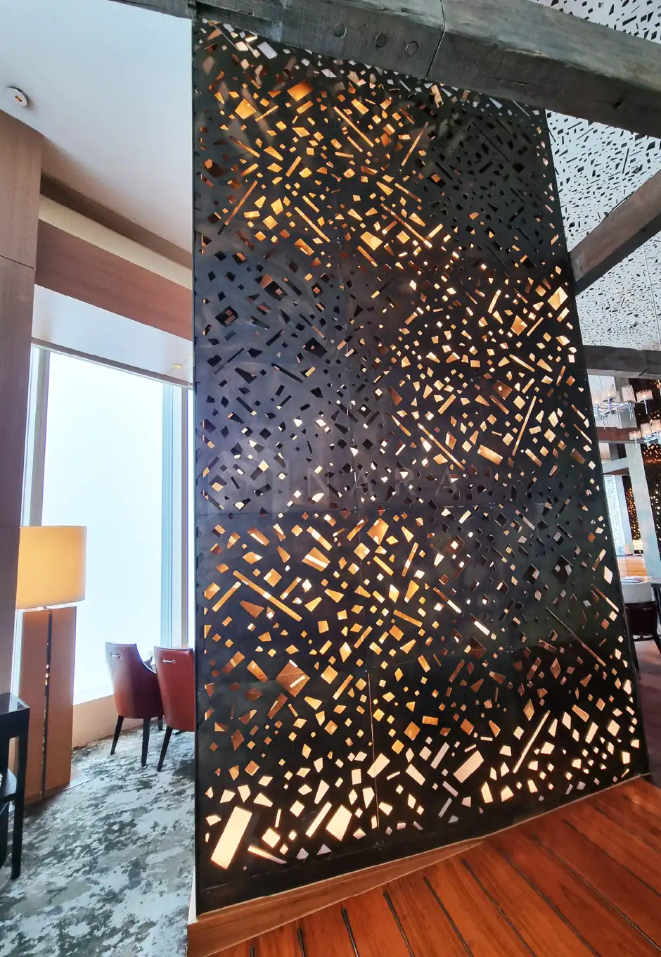Reflective gold stainless steel decorative partition with intricate cut-out patterns, enhancing modern interior design and ambiance in a stylish restaurant or hotel setting.