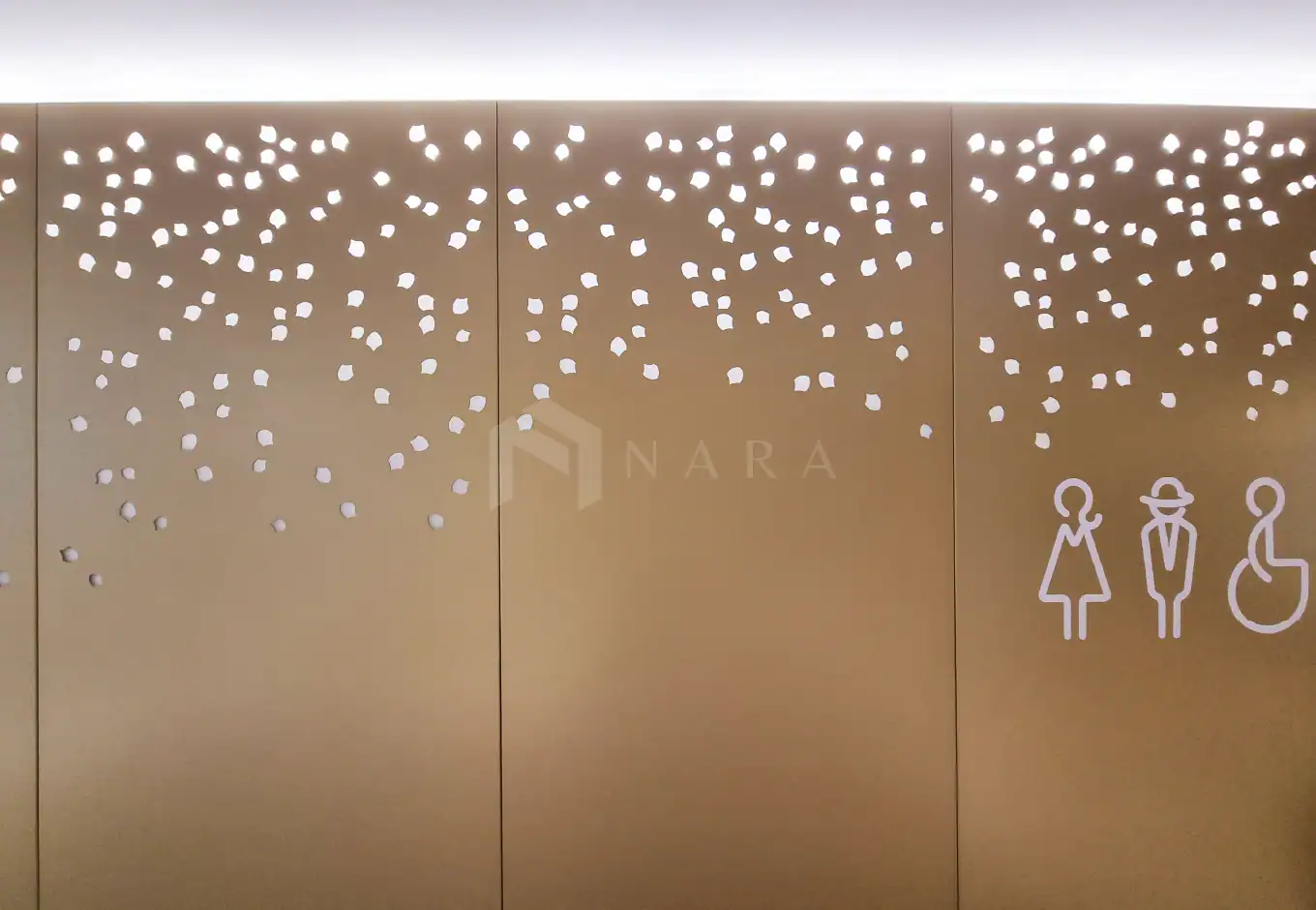 Shiny gold stainless steel wall panel with decorative perforations and handicapped restroom icons, creating an elegant and functional design element for modern facilities.