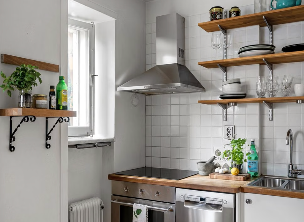 Modern kitchen with stainless steel appliances, wooden shelves, and white tiled walls, featuring green plants and kitchenware.