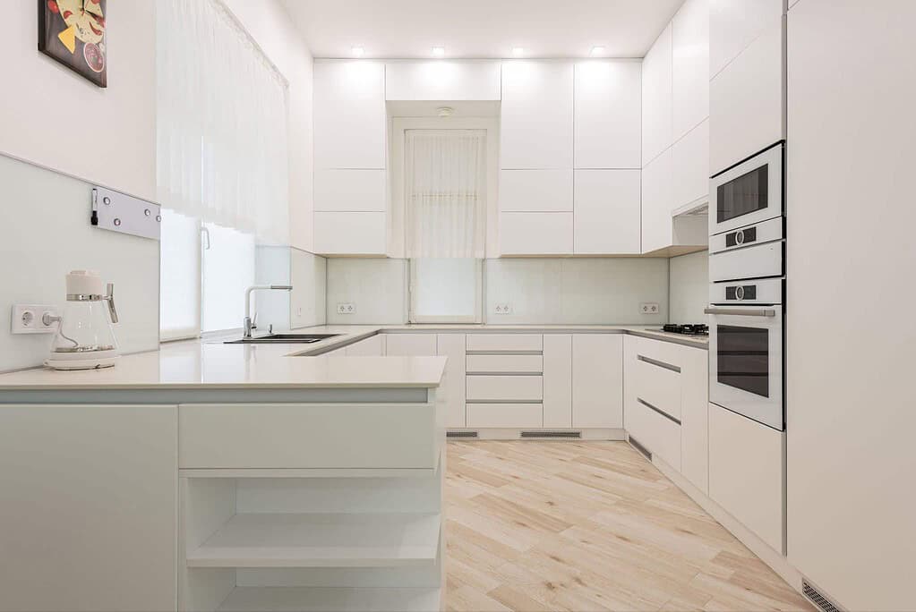 Modern white kitchen with sleek cabinetry, built-in appliances, and light wood flooring, featuring minimalist design and ample natural light.