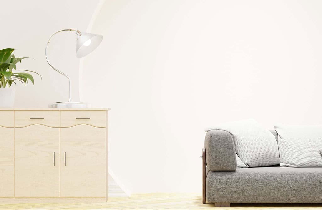 Modern living room with a light-colored wooden cabinet, a white desk lamp, and a gray sofa against a white wall.