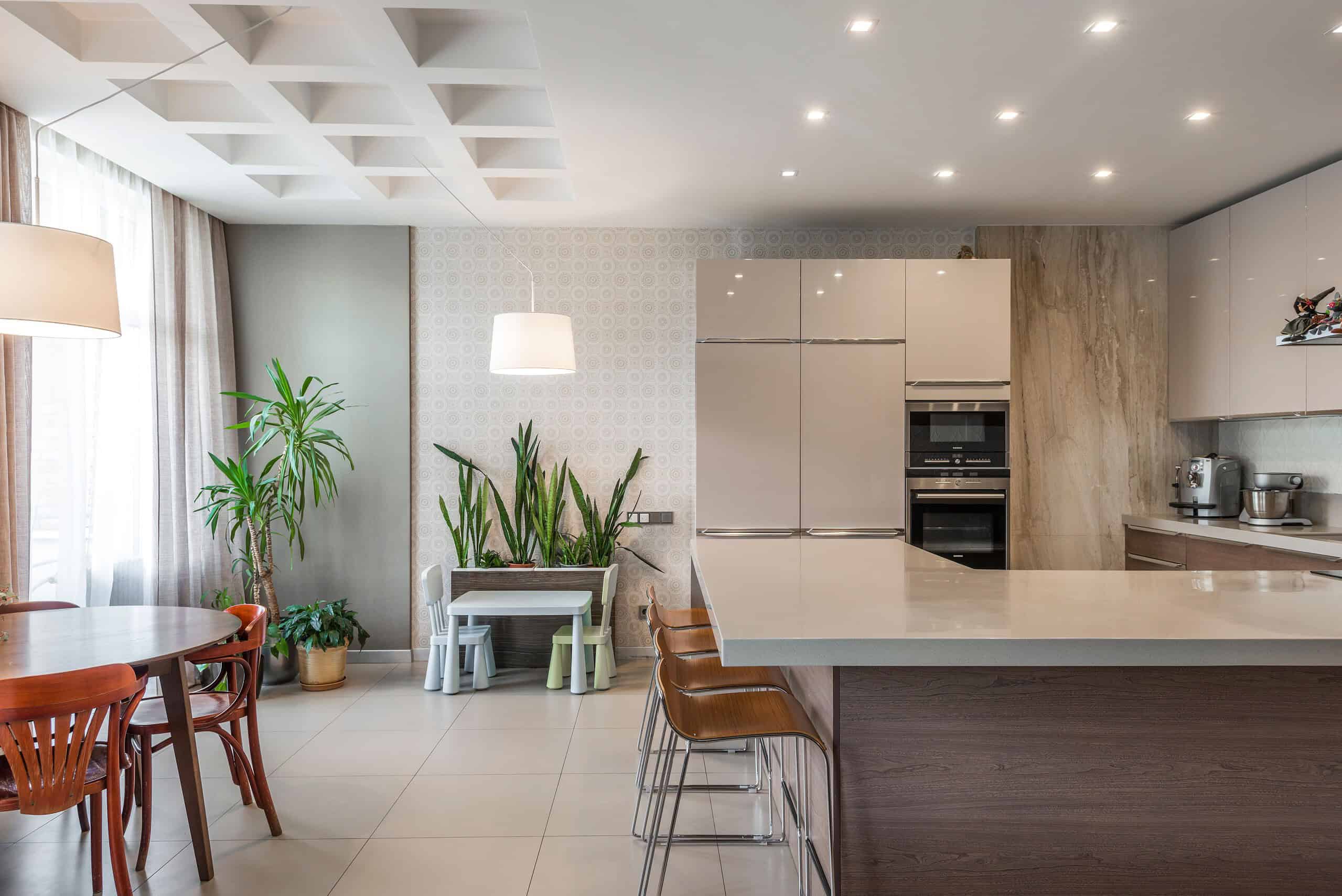 Modern kitchen with beige cabinets, marble backsplash, and a large island with brown bar stools, featuring sleek stainless steel appliances and ambient lighting.